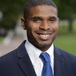 Headshot of Quinton Smith. He is wearing a navy blue suit, white collared shirt, and light blue tie.