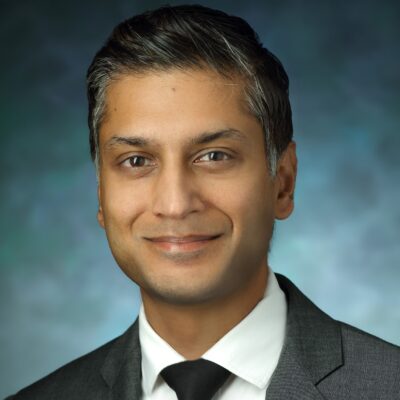 Headshot of Sashank Reddy. He has short, salt and pepper hair and brown eyes. He is wearing a gray suit jacket, white button down dress shirt, and black tie.