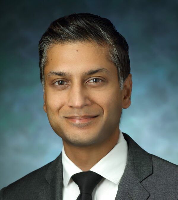 Headshot of Sashank Reddy. He has short, salt and pepper hair and brown eyes. He is wearing a gray suit jacket, white button down dress shirt, and black tie.