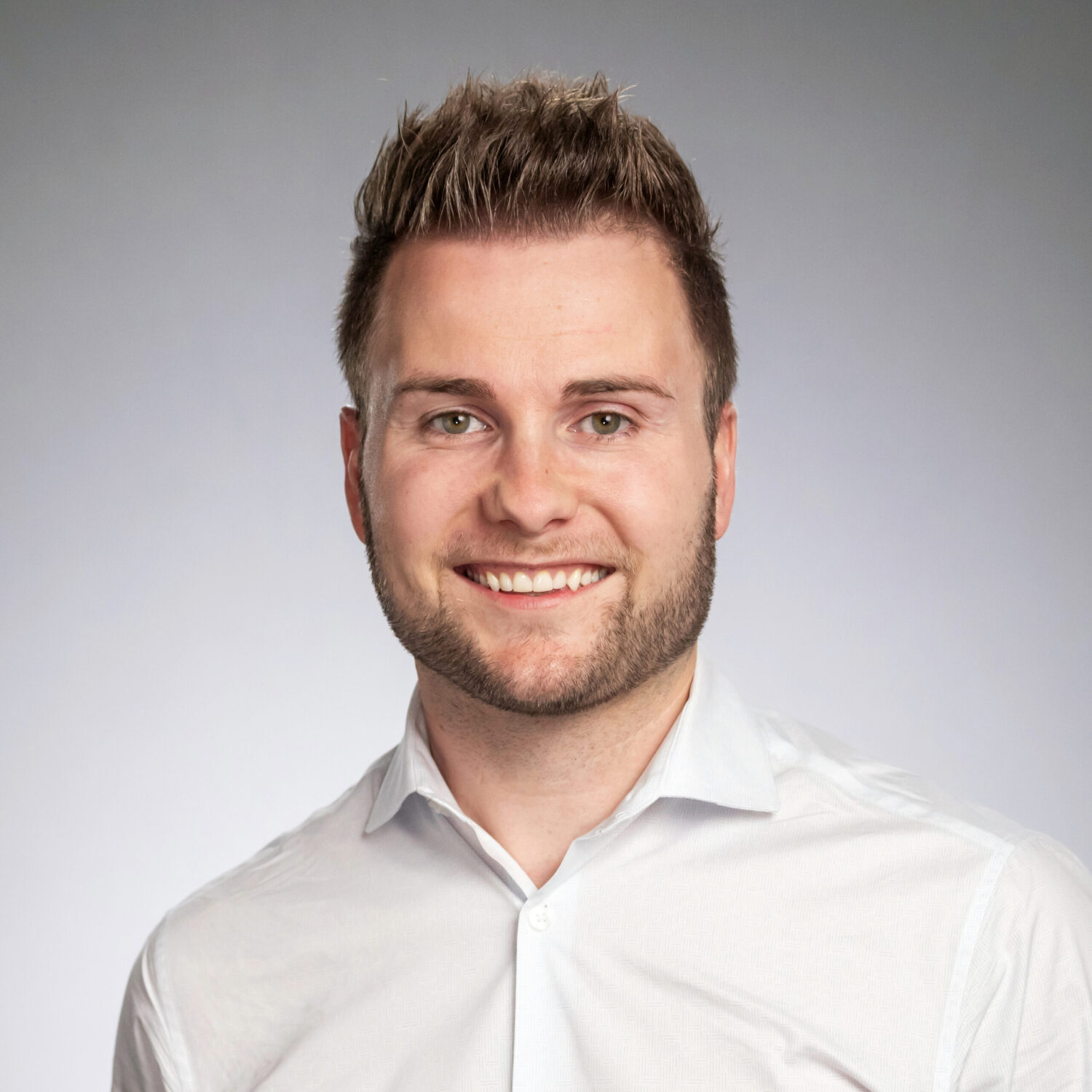 Headshot of Jochen Mueller. He is wearing a white button down collared shirt and standing in front of a white and gray background.