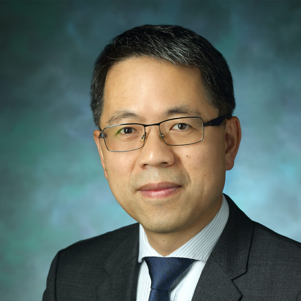 Headshot of Hai-Quan Mao. He has salt and pepper short hair and is wearing square, black framed glasses. He is also wearing a blue and white horizontal striped shirt, dark blue tie, and gray suit jacket.