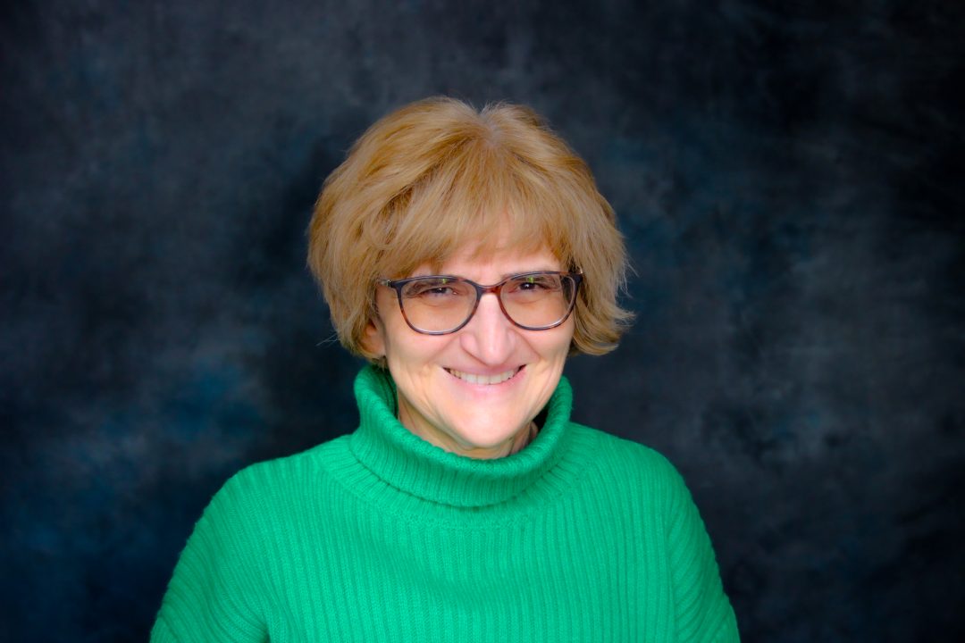 Headshot of Kalina Hristova. She is wearing a green turtleneck sweater and black square rimmed glasses. She has light skin tone, cheekbone length blonde hair with bangs, and dark color eyes.