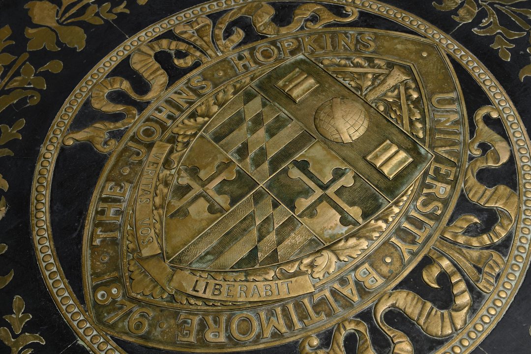 Closeup photograph of Johns Hopkins seal. It is on the floor in gold and black.