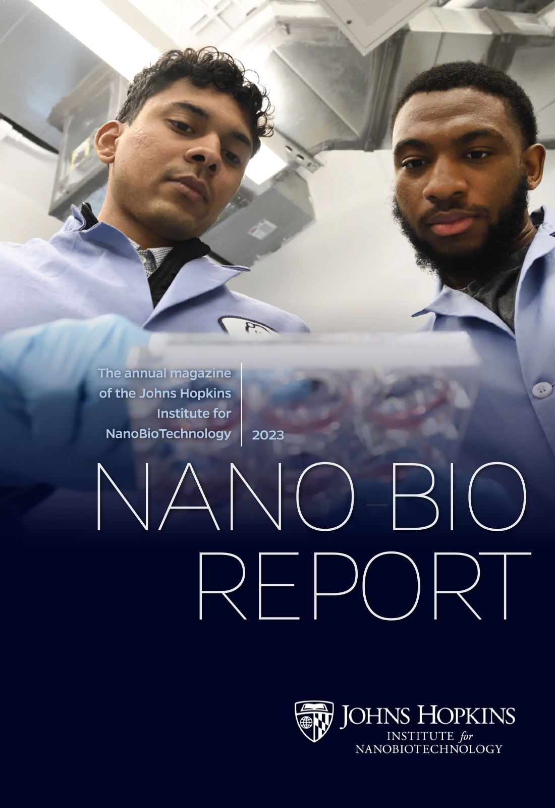 Magazine cover. The text reads, The annual magazine of the Johns Hopkins Institute for NanoBioTechnology, 2023, Nano-Bio Report. The image is of two males in blue lab coats looking at a cell well.