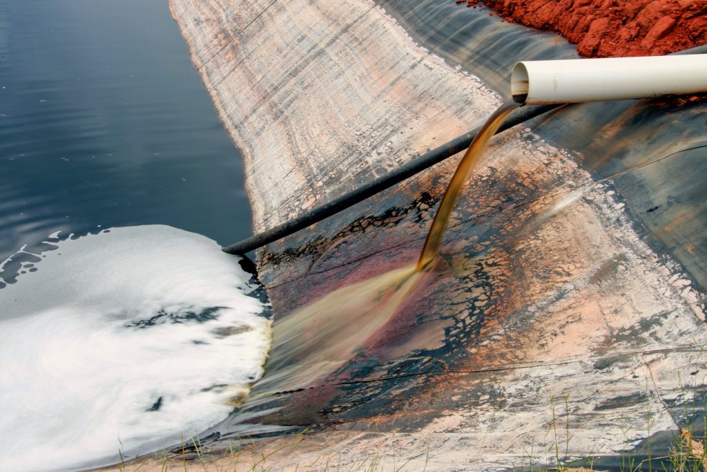 Leachate pond. On the right a dark liquid is coming out of a white pipe into a plastic lined-pond.