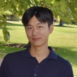 Headshot of Heonjoon Lee. He has dark eyes and short black hair with bangs. He is wearing a dark blue polo shirt and standing under a tree in front of a campus quad.