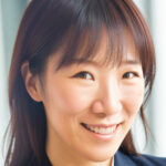 Headshot of Yun Chen. She brown, almond-shaped eyes and long brown hair with bangs. She is wearing a black collared blazer over a white collared shirt.