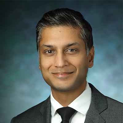 Headshot of Sashank Reddy. He has short, salt and pepper hair and brown eyes. He is wearing a gray suit jacket, white button down dress shirt, and black tie.