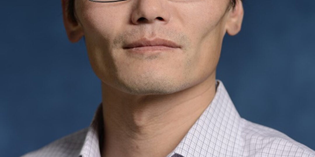 Headshot of Sean Sun. He has short black hair, dark, almond-shaped brown eyes, and light skinned. He is wearing a white dress shirt with a checkered patter and black square frame glasses.