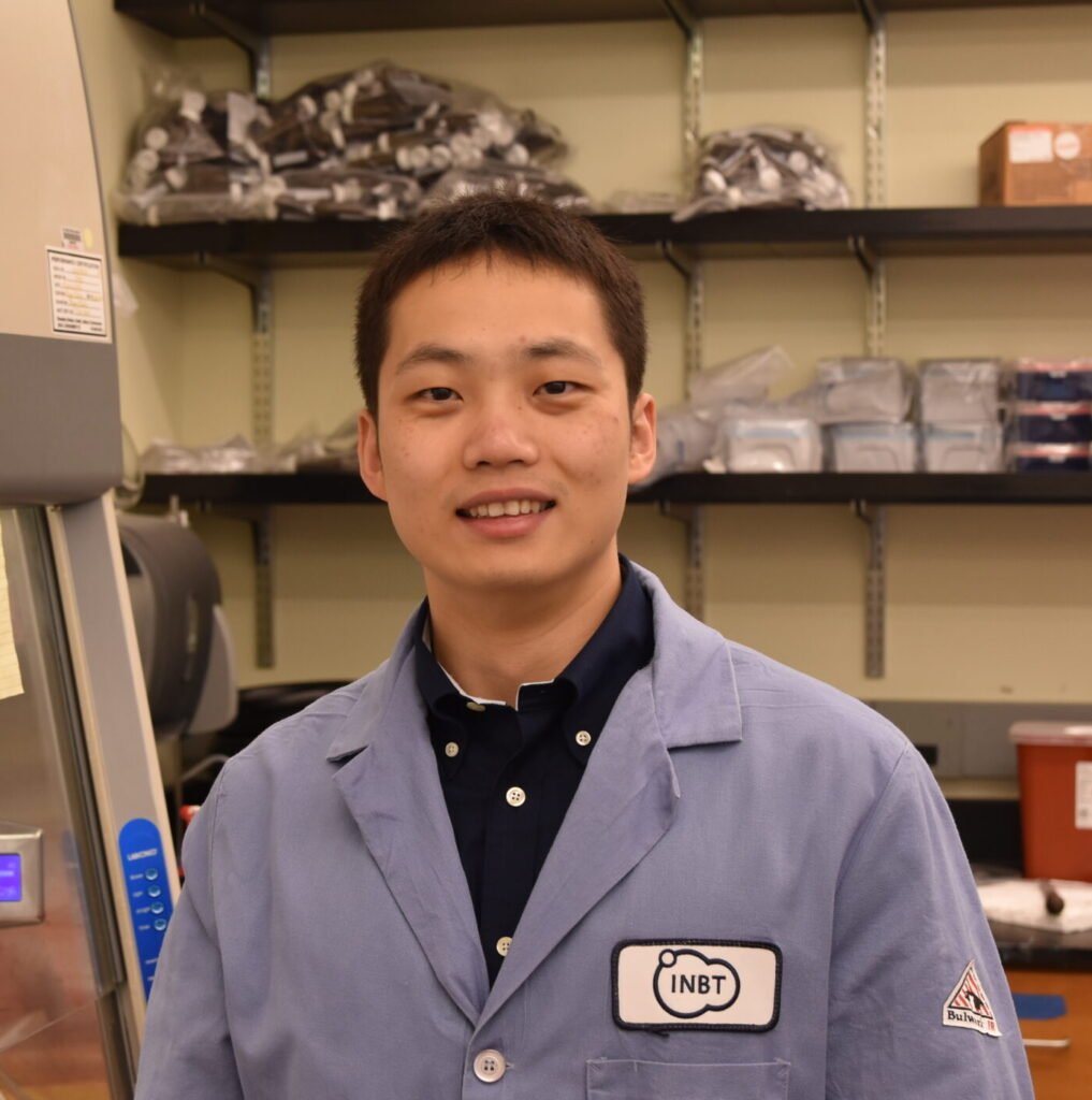 Gene Fu in a lab coat smiling with a lab background.