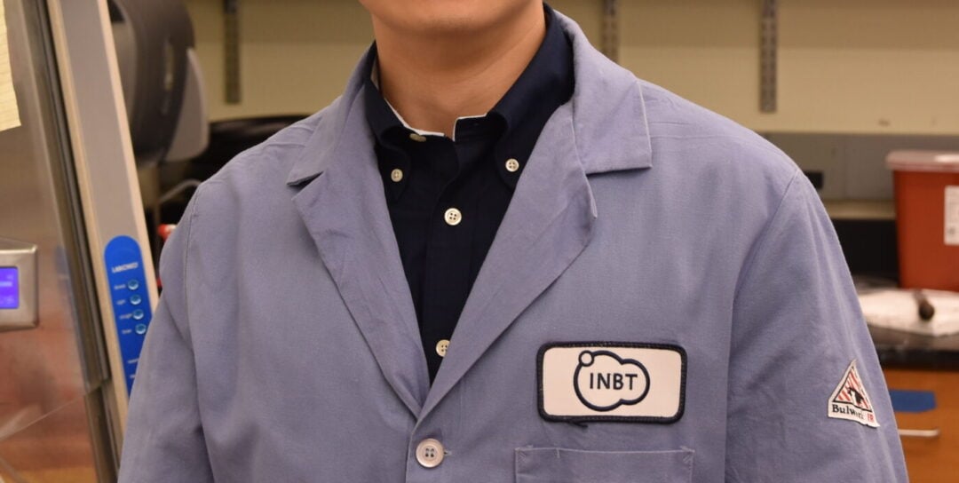Gene Fu in a lab coat smiling with a lab background.