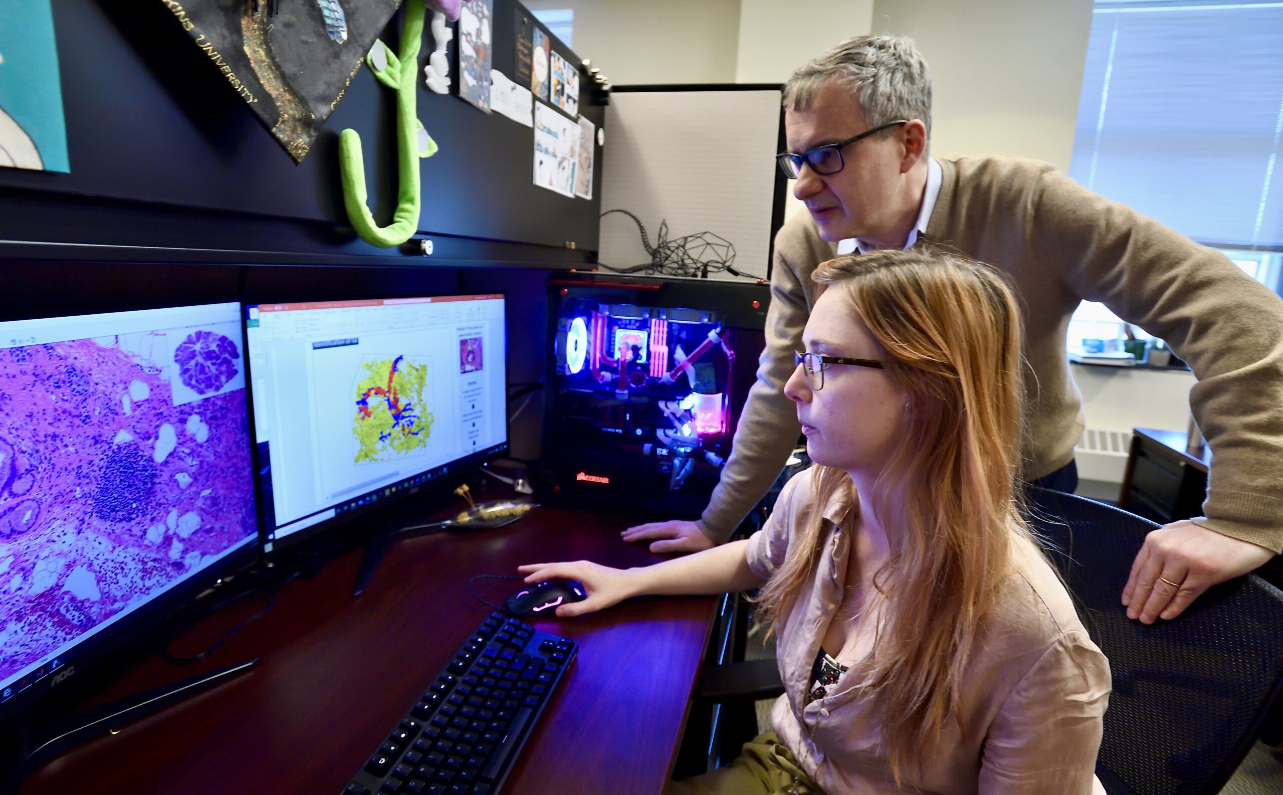 A man and woman looking at two computer screens of microscopy images.