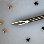 Zoomed in photo of metal six metal grippers shaped liked stars next to 18 gauge need for scale reference.